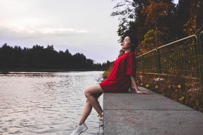 Young woman looking away while sitting by tree against sky