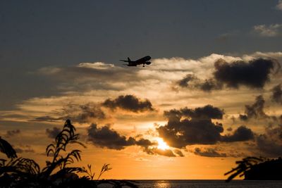 Silhouette airplane flying over sea against sky during sunset