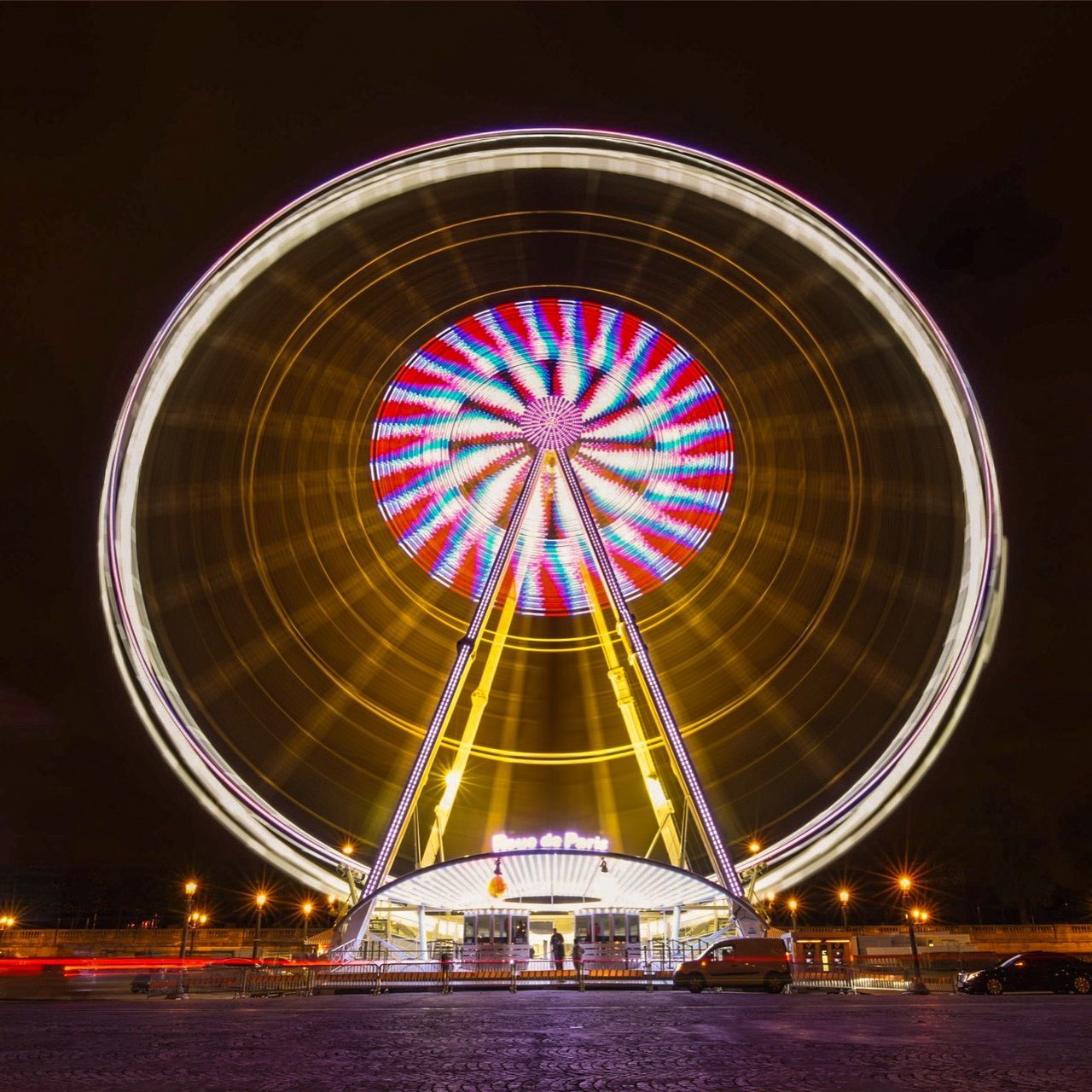 illuminated, night, arts culture and entertainment, ferris wheel, amusement park, amusement park ride, circle, multi colored, built structure, architecture, lighting equipment, low angle view, motion, sky, glowing, long exposure, outdoors, geometric shape, no people, pattern