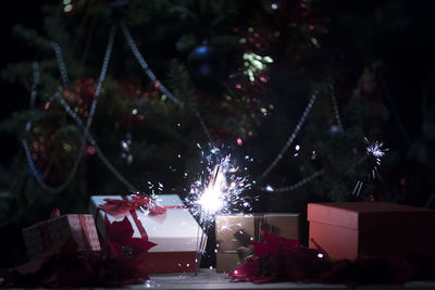 Close-up of illuminated sparkler by christmas tree at night