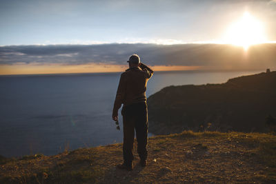 Rear view of man standing on mountain at sunset