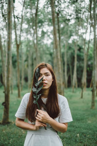 Young woman holding leaves while standing in forest