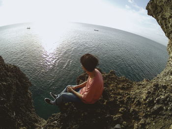 Man sitting on rock by sea against sky