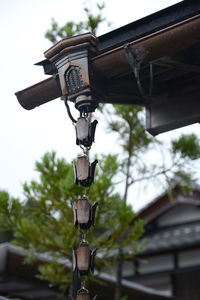 Low angle view of electric lamp hanging by building against sky