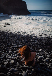 Woman on rock at beach against sky