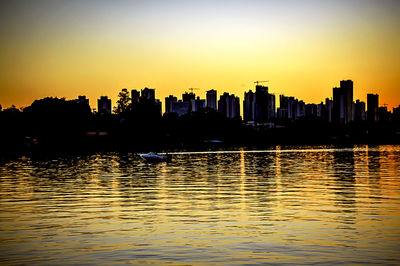 Silhouette of city at waterfront during sunset