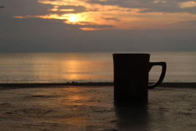 Coffee cup on table against sea during sunset