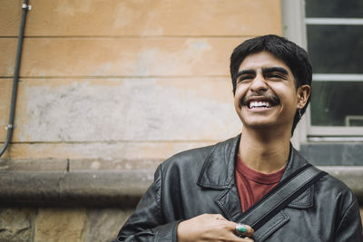 Low angle view of cheerful boy laughing against wall