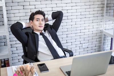 Full length of man using mobile phone while standing against wall