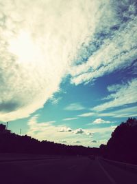 Road by silhouette trees against sky