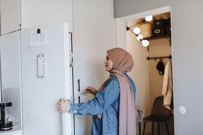 Smiling woman at home opening fridge