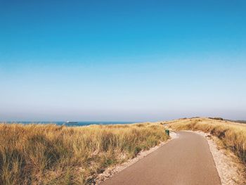 Scenic view of road by sea against clear blue sky