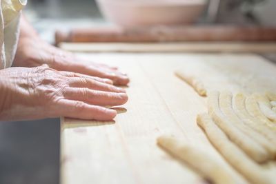 Cropped hands rolling dough at table in kitchen