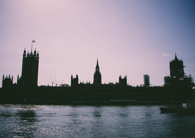 Silhouette buildings by river against sky in city