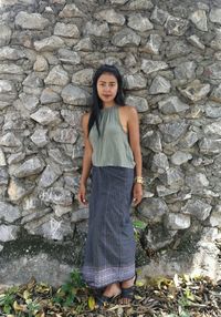 Portrait of beautiful young woman standing against stone wall