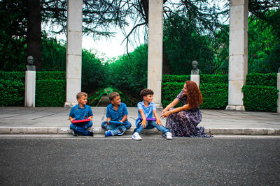 Woman and children sitting by footpath against park