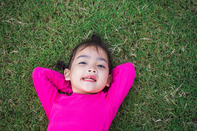 Portrait of smiling cute girl with hands behind head lying on grass at park