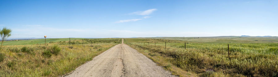Dirt road amidst field against sky