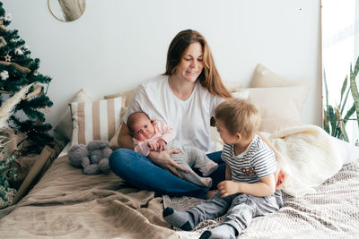 A young mother with two small children spends time in the bedroom at home.