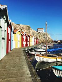 Boats moored at harbor against clear blue sky