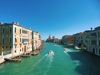 Boats in canal amidst buildings against clear blue sky