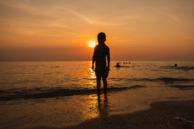 Rear view of silhouette man standing on beach during sunset