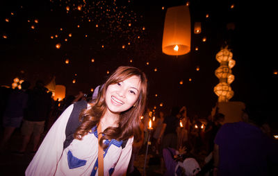 Portrait of smiling woman standing against paper lanterns at night