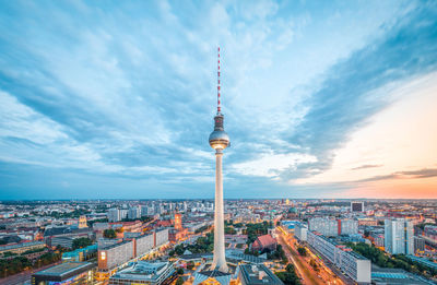 Television tower in city against cloudy sky during sunset