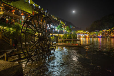 Illuminated footbridge over river against sky at night