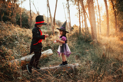 Girl wearing witch hat standing with brother at forest during halloween