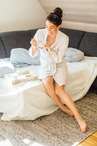 High angle view of young woman having coffee while sitting on bed at home