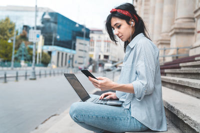 Side view of young woman using mobile phone in city