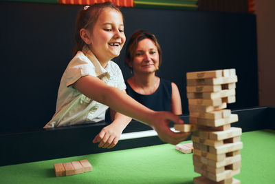 Excited girl playing jenga game with her mom in play room. girl removing one block from blocks tower