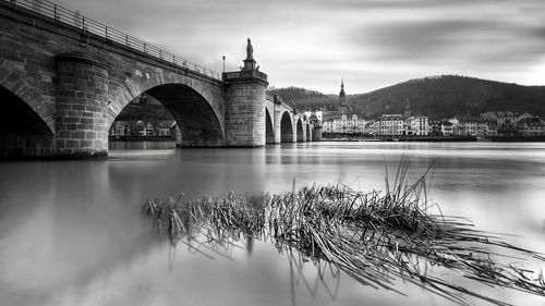 Arch bridge over river against cloudy sky