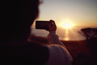 Rear view of man photographing against sky during sunset