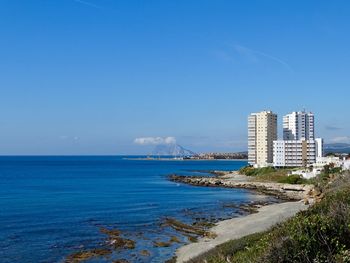 Scenic view of sea by buildings against blue sky