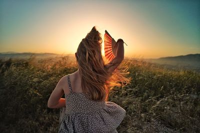 Rear view of girl standing on field against sky during sunset