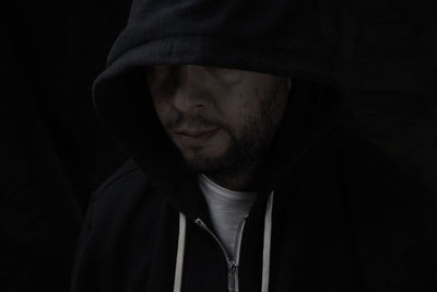 Close-up of man in hood against black background