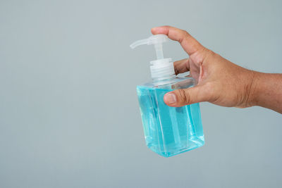 Close-up of hand holding bottle against blue background