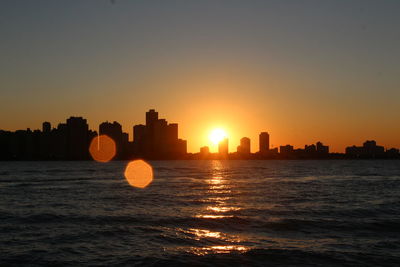 Silhouette buildings by sea against sky during sunset