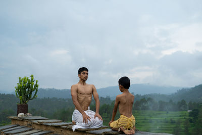 Friends sitting on rock against sky