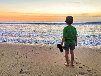 Rear view of boys on beach against sky during sunset