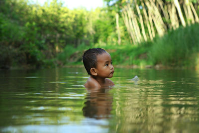 Cute boy swimming in pond against trees