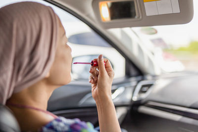 Woman looking in rear view mirror painting her lips doing applying make up in car