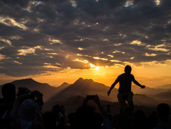 Silhouette people photographing on mountain during sunset