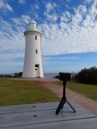 Lighthouse on field by building against sky