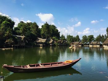 Boats moored on river by trees against sky