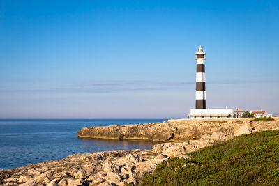 Lighthouse amidst sea and buildings against sky