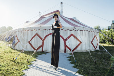 Male artist in costume standing on stilts in front of circus tent