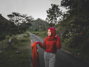 Portrait of smiling young woman standing against trees